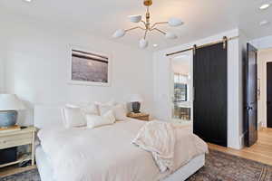 Primary Bedroom with hardwood / wood-style floors, a barn door, and an inviting chandelier