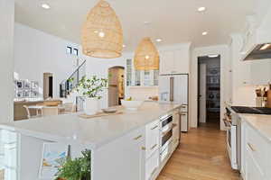 Kitchen with custom exhaust hood, white appliances, a center island, white cabinetry, and hanging light fixtures