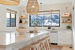 Kitchen featuring white dishwasher, plenty of natural light, pendant lighting, and white cabinetry