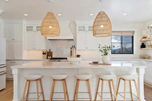 Kitchen with white cabinetry, a kitchen bar, decorative backsplash, a kitchen island, and custom exhaust hood