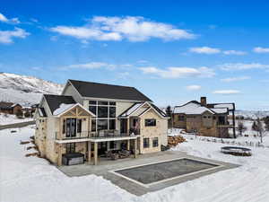 Snow covered back of property with a mountain view, a balcony, and swimming pool