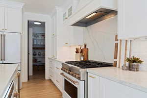 Kitchen with high end range, tasteful backsplash, white cabinets, and custom exhaust hood