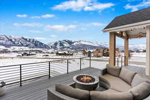 Snow covered deck featuring a mountain view and an outdoor living space with a fire pit