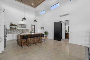 Kitchen with a wall mounted air conditioner, a high ceiling, white cabinets, hanging light fixtures, and a barn door