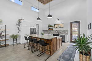 Kitchen featuring hanging light fixtures, a kitchen island, stainless steel refrigerator with ice dispenser, a towering ceiling, and white cabinets