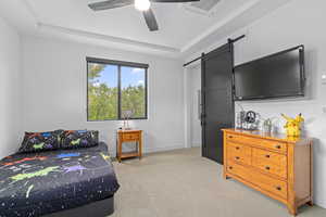 Bedroom featuring a raised ceiling, ceiling fan, a barn door, and light colored carpet