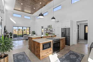 Kitchen with appliances with stainless steel finishes, wood ceiling, a high ceiling, a kitchen island, and hanging light fixtures