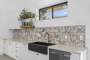 Kitchen featuring dishwasher, decorative backsplash, white cabinets, and sink