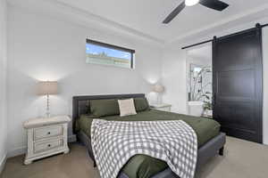 Bedroom featuring a barn door, light colored carpet, and ceiling fan