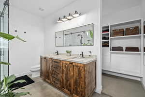 Bathroom featuring vanity, toilet, a shower, and concrete floors