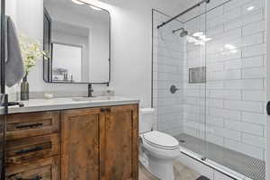 Bathroom featuring tiled shower, vanity, and toilet