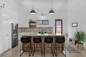 Kitchen featuring a kitchen bar, decorative light fixtures, stainless steel fridge with ice dispenser, a center island, and white cabinetry