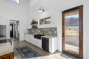 Kitchen with a mountain view, sink, black dishwasher, tasteful backsplash, and white cabinetry