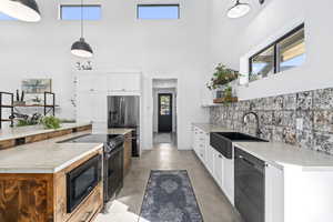 Kitchen with black appliances, white cabinetry, sink, and hanging light fixtures