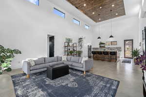 Living room with concrete flooring, a healthy amount of sunlight, a towering ceiling, and wood ceiling