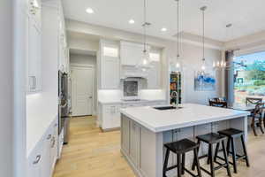 Kitchen with white cabinetry, sink, a chandelier, pendant lighting, and a kitchen island with sink