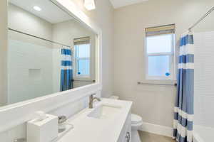 Full bathroom with vanity, shower / bathtub combination with curtain, toilet, and plenty of natural light