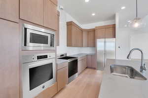 Kitchen with tasteful backsplash, sink, pendant lighting, built in appliances, and light hardwood / wood-style flooring