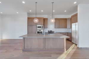 Kitchen featuring built in appliances, a center island with sink, backsplash, and sink