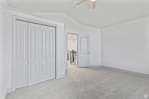 Unfurnished bedroom with light carpet, a closet, vaulted ceiling, and ceiling fan