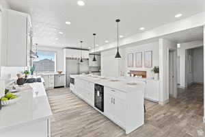 Kitchen with beverage cooler, built in appliances, decorative light fixtures, white cabinets, and a kitchen island