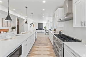 Kitchen with white cabinets, pendant lighting, wall chimney exhaust hood, and double oven range