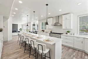 Kitchen featuring a kitchen island, double oven range, wall chimney range hood, and white cabinetry