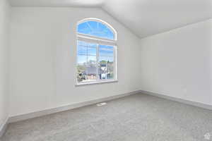 Spare room with plenty of natural light, carpet floors, and vaulted ceiling