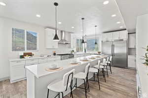 Kitchen with high end appliances, wall chimney range hood, a center island, white cabinetry, and hanging light fixtures