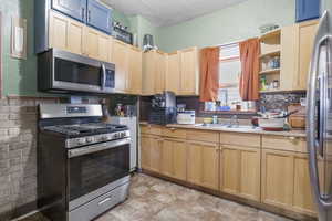 Kitchen featuring light brown cabinets, a textured ceiling, stainless steel appliances, and sink