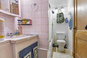 Full bathroom with hardwood / wood-style flooring, vanity, bath / shower combo with glass door, and tile walls