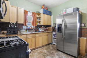 Kitchen with light brown cabinets, backsplash, sink, stainless steel refrigerator with ice dispenser, and a textured ceiling