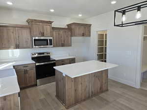 Kitchen with decorative light fixtures, a kitchen island, appliances with stainless steel finishes, and light hardwood / wood-style flooring