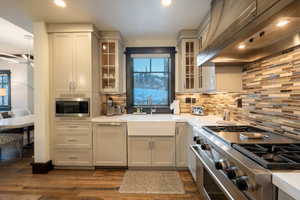 Kitchen featuring ventilation hood, white cabinets, sink, dark hardwood / wood-style flooring, and stainless steel appliances