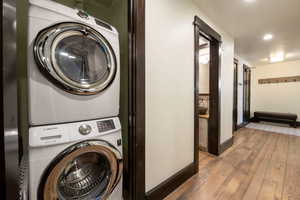 Clothes washing area featuring hardwood / wood-style floors and stacked washing maching and dryer