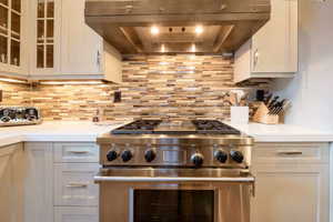 Kitchen with white cabinets, high end stove, ventilation hood, and tasteful backsplash