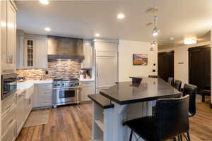 Kitchen featuring a breakfast bar, decorative backsplash, built in appliances, and wall chimney exhaust hood