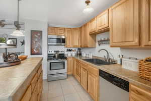 Kitchen with tile countertops, sink, hanging light fixtures, light tile patterned floors, and stainless steel appliances