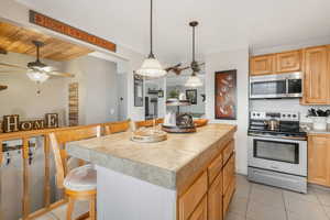 Kitchen with a center island, a kitchen breakfast bar, ceiling fan, light brown cabinetry, and appliances with stainless steel finishes