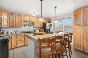 Kitchen with black range with electric stovetop, a breakfast bar, sink, light tile patterned floors, and a kitchen island