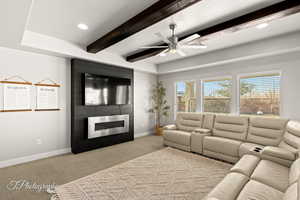 Carpeted living room featuring beam ceiling, ceiling fan, and a large fireplace