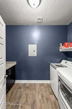 Clothes washing area with hardwood / wood-style floors, a textured ceiling, electric panel, and washer and clothes dryer