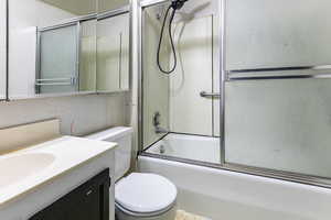 Full bathroom with decorative backsplash, vanity, toilet, and enclosed tub / shower combo