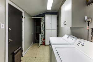 Laundry room featuring washer and dryer, electric panel, cabinets, and radiator