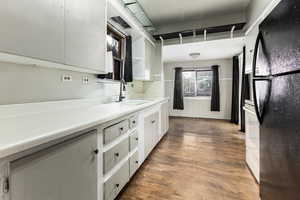 Kitchen with white cabinetry, black fridge, dark wood-type flooring, and sink