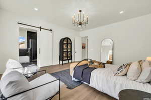 Bedroom with a barn door, light wood-type flooring, and a chandelier