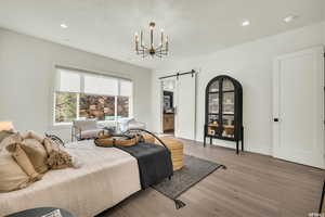 Bedroom featuring wood-type flooring, a barn door, ensuite bath, and a notable chandelier