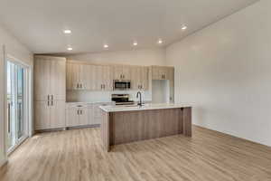 Kitchen with light brown cabinets, a center island with sink, sink, light wood-type flooring, and stainless steel appliances