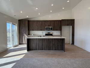 Kitchen with vaulted ceiling, light countertops, dark brown cabinetry, and stainless steel appliances