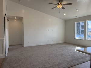 Empty room featuring baseboards, visible vents, ceiling fan, a barn door, and light colored carpet